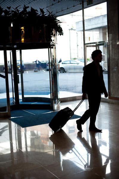 Man entering hotel lobby with his luggage. Car parked in the background